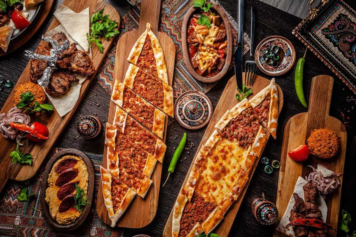Overhead shot of a table dotted with pide – a canoe-shaped Turkish equivalent of pizza – alongside other platters of meat cutlets and side dishes