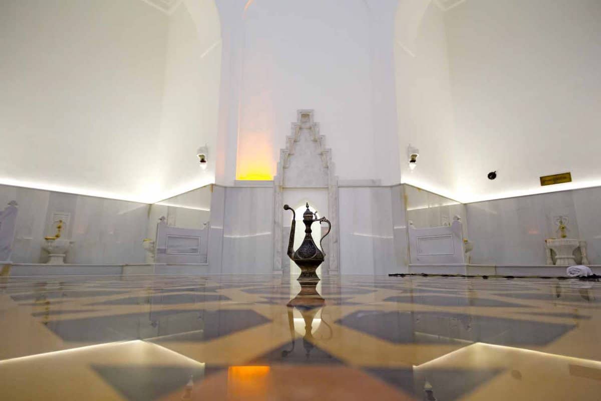 Brass water jug resting on the marble floor of a white, cavernous room inside a bathhouse