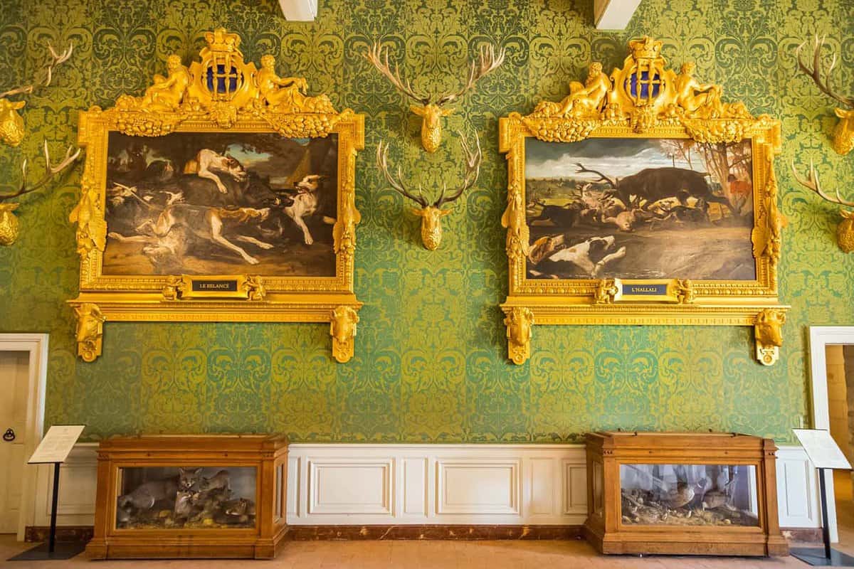 A green wall with two large, gold-framed paintings on the wall