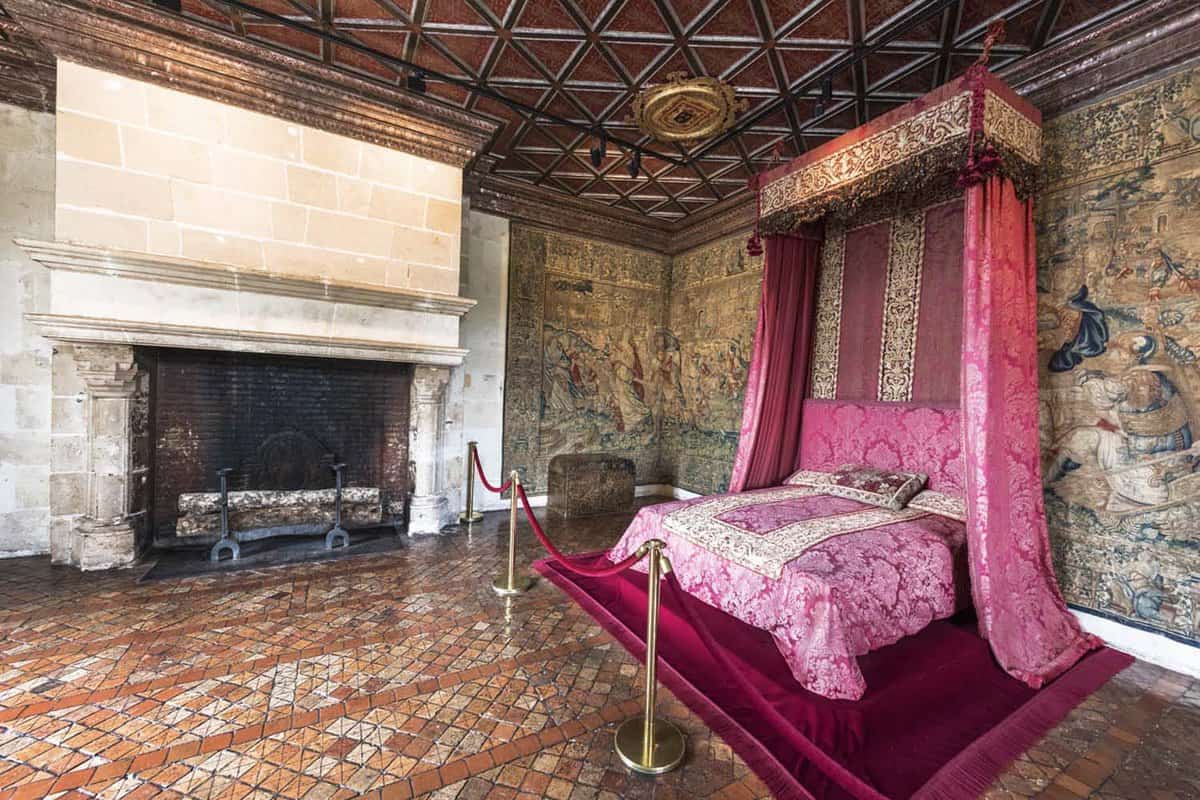 A bedroom with pink bed and curtains with large stone fireplace