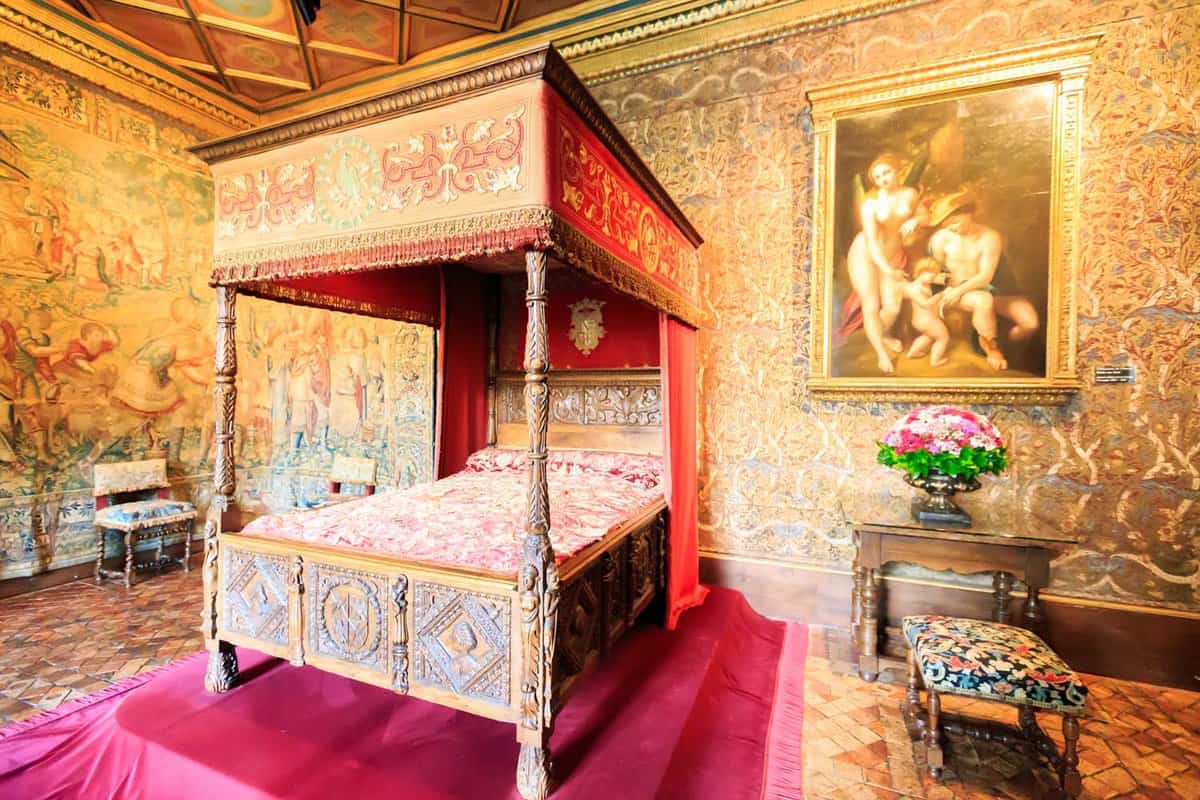 An ornate bedroom with four-poster single bed and paintings for wallpaper