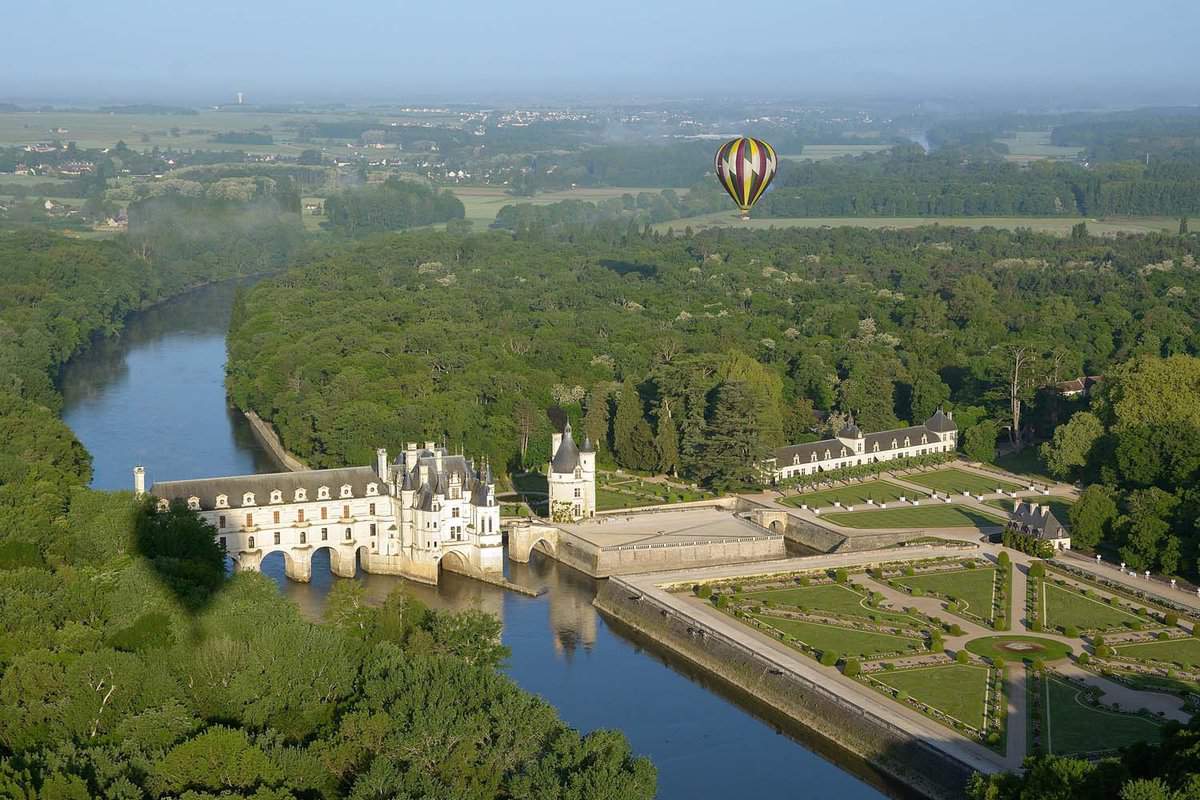 A single hot air balloon flying over the forests surrounding Loire Castle, during a bright yet misty day