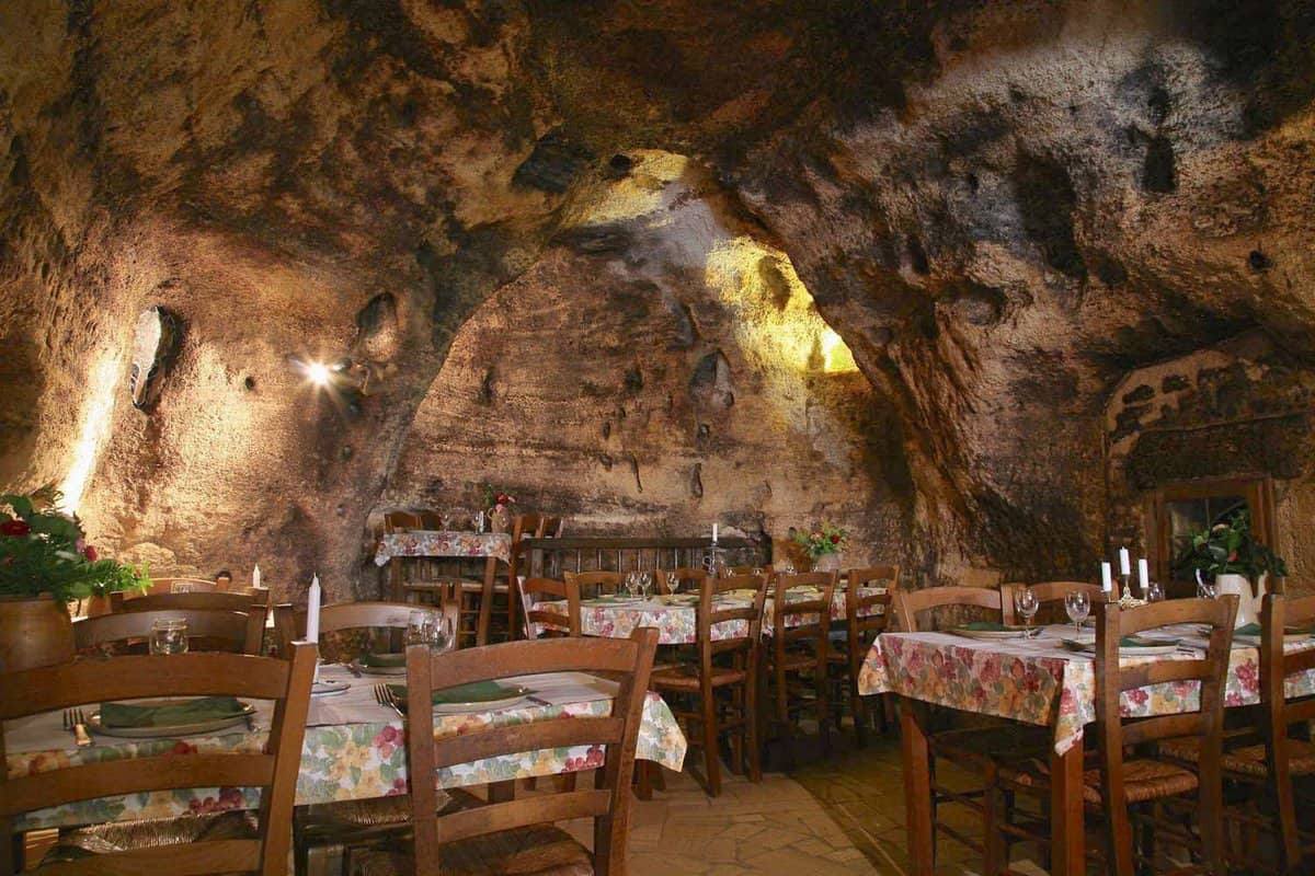 Interior of a lighted cave housing a tables and chairs of a restaurant