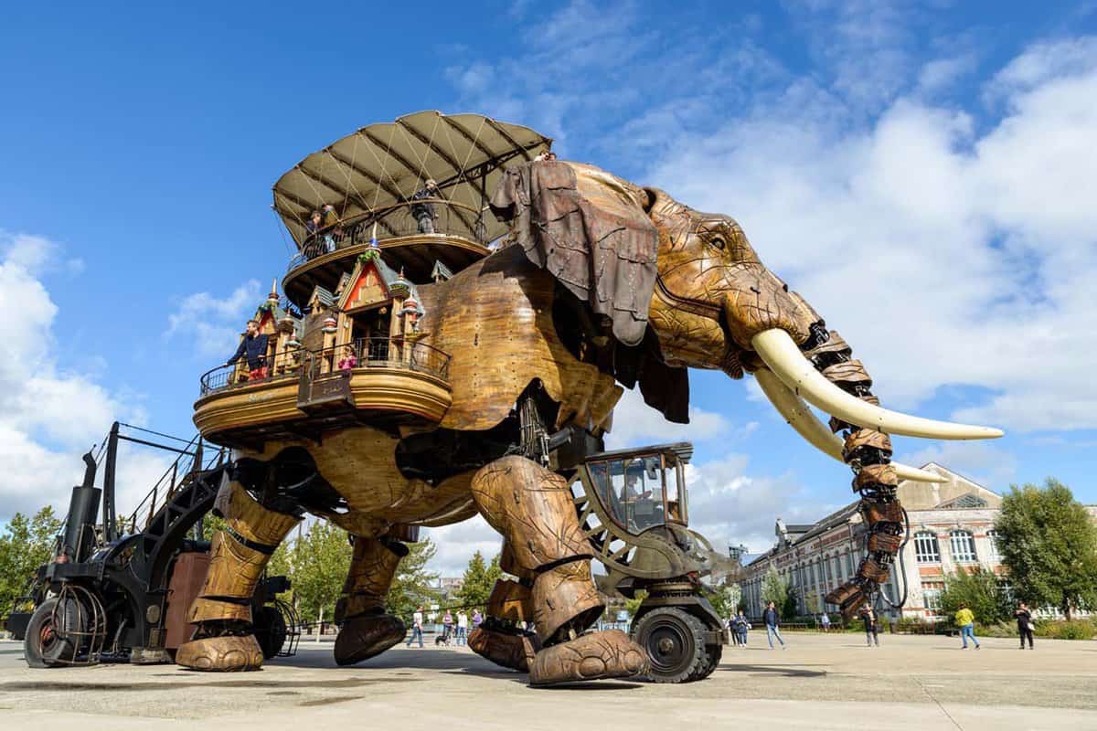 A huge mechanical elephant with a wooden exterior at Machines de l’Île, with tourists walking inside the small balcony area