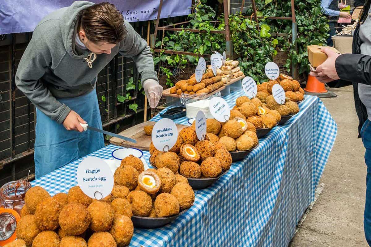 A man preparing scotch eggs for a customer during the daytime