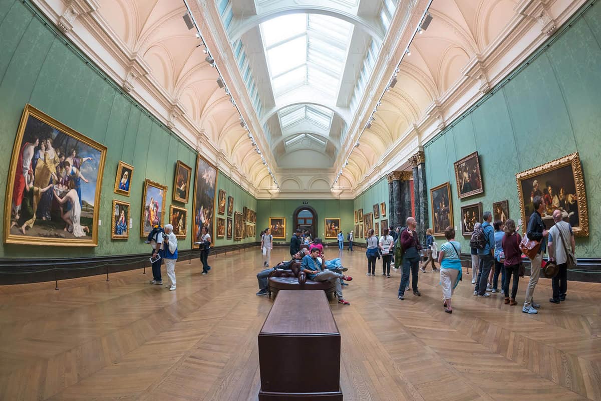 Interior gallery will walls covered in gold-framed paintings