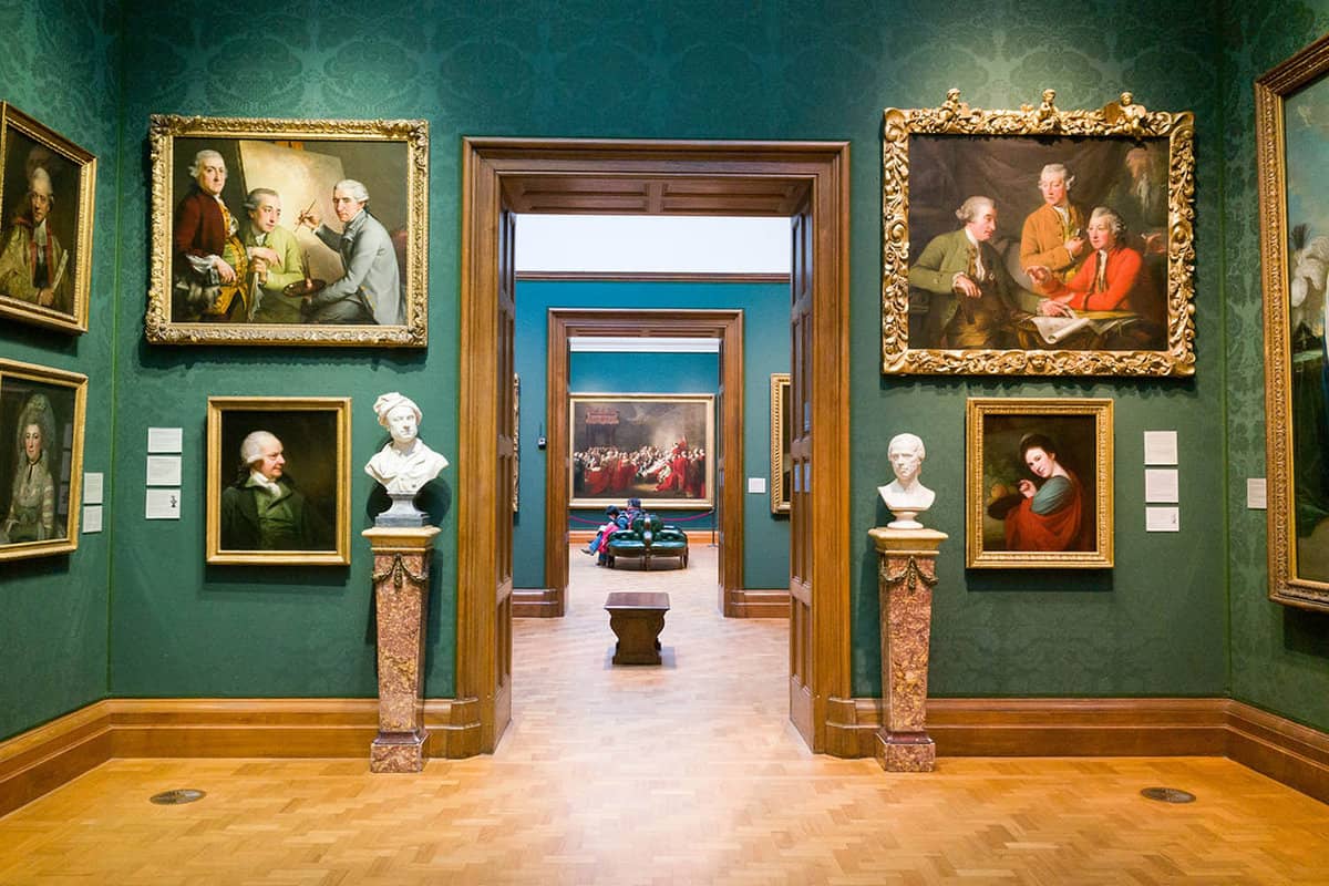 A display room with green walls covered in gold-framed art leading to other display rooms
