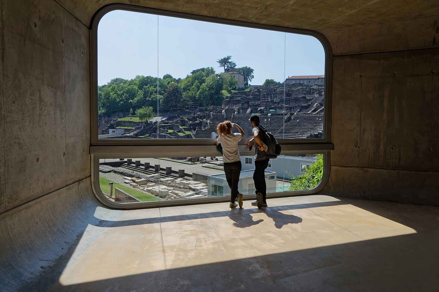 Two tourists looking through a window in the museum out to the amphitheater