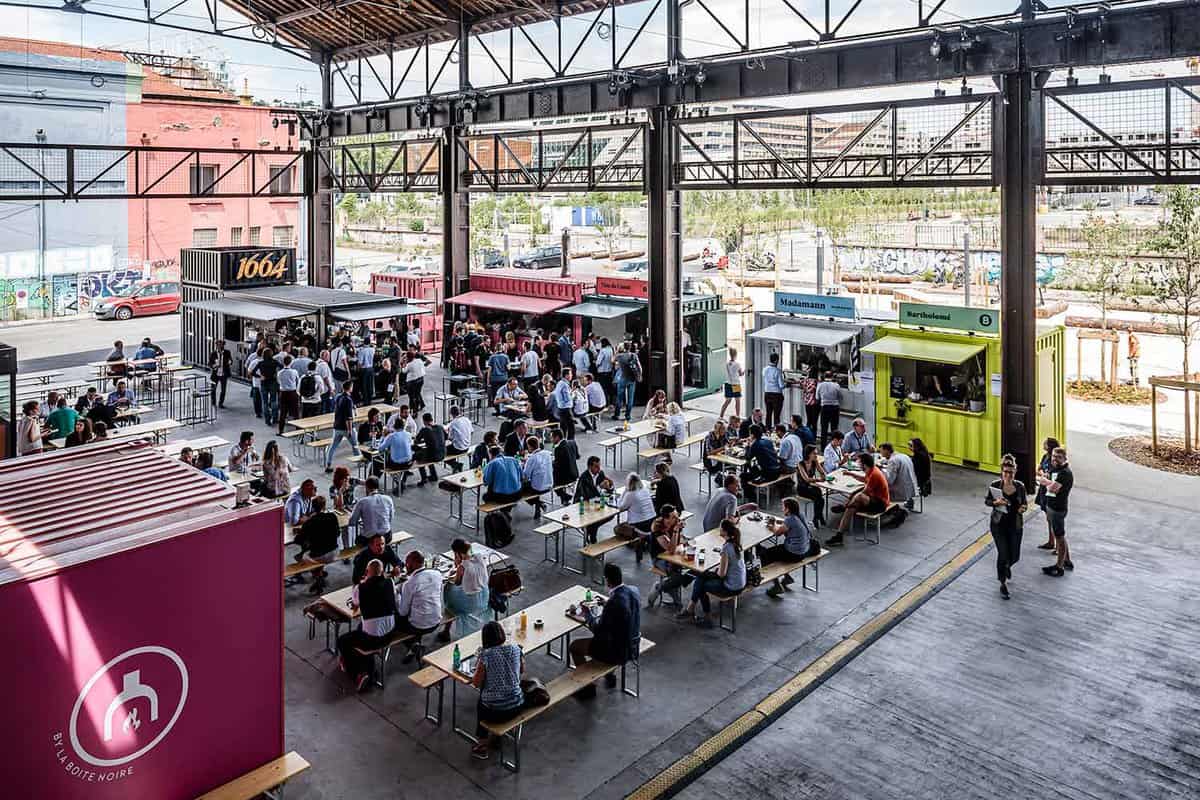 A large warehouse filled with tables and lots of people eating at them