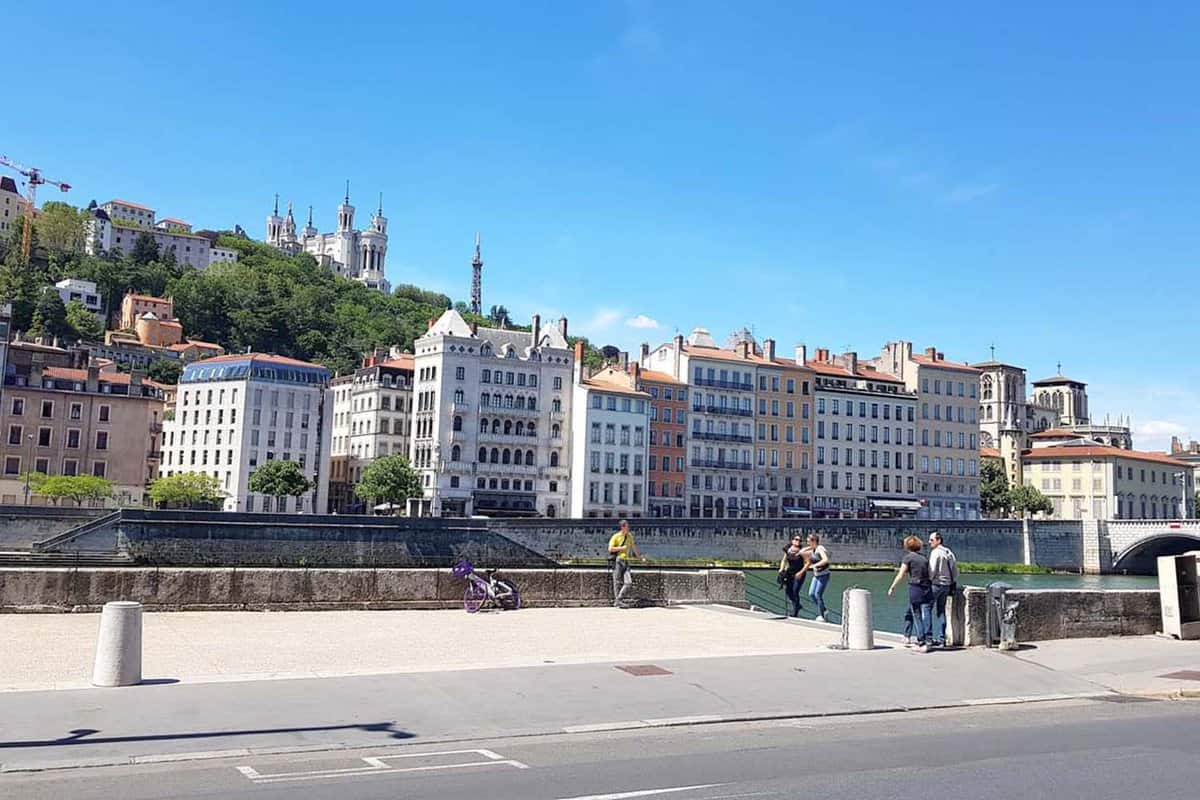 People walking by the the Saone river. The area has the view of the Basilica of Notre-Dame de Fourvière,