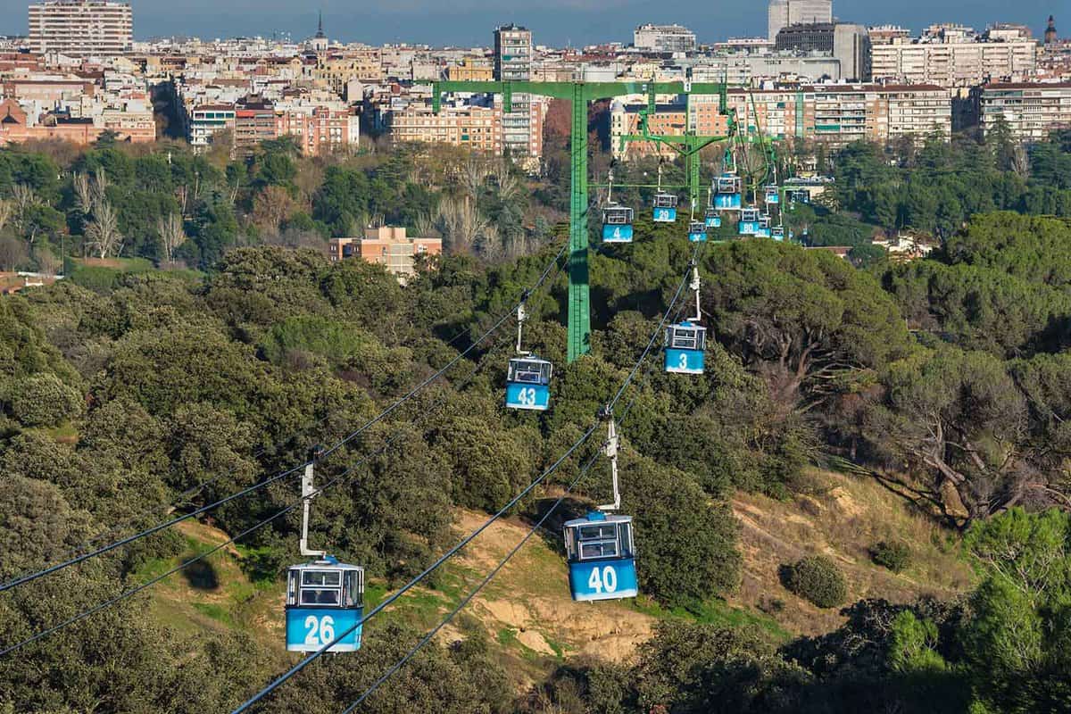Cable car over casa de campo park in Madrid, Spain. The blue cable cars are above the trees in the park, with the city visible in the background.