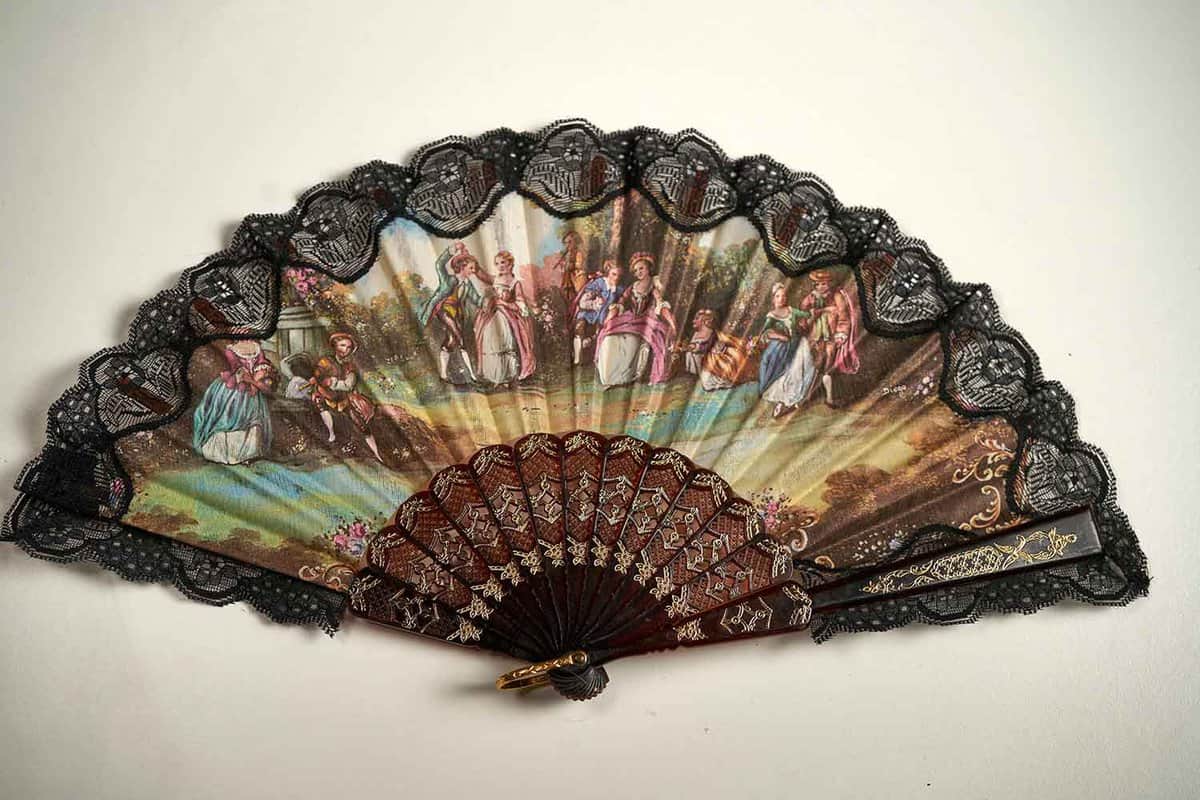 A traditional Spanish hand fan - black lace on top of the fan fabric which shows a pastoral scene.