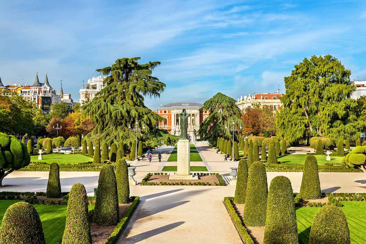 The Parterre garden in Buen Retiro Park. Shaped topiary shrubbery, trimmed lawns, trees, and white pathways fill this park.