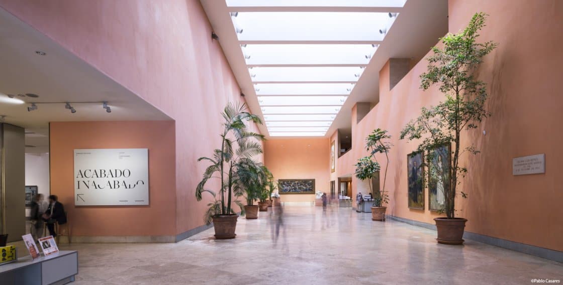 Inside the Thyssen-Bornemisza Museum. Dusky pink walls, polished floors, and plants decorate the interior, and there is a row of large skylights.