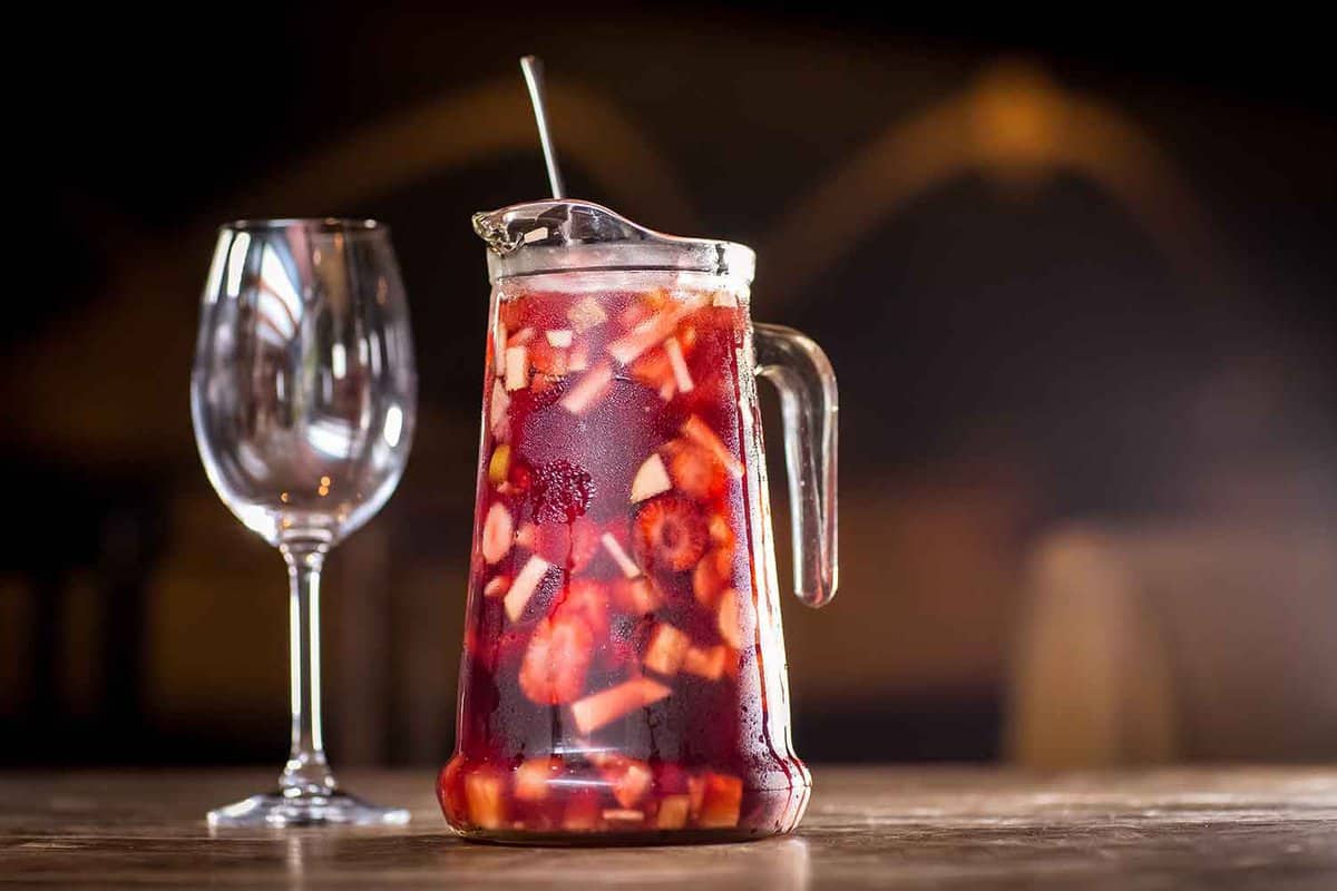 A glass jug of sangria accompanied by a glass on a wooden table