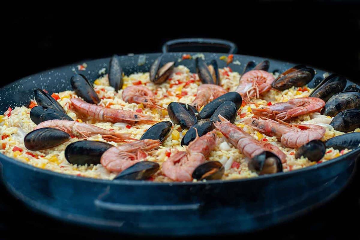 Seafood paella in a large frying pan at a street food festival. Whole shrimps and mussels are arranged in a circle on top of the rice dish.