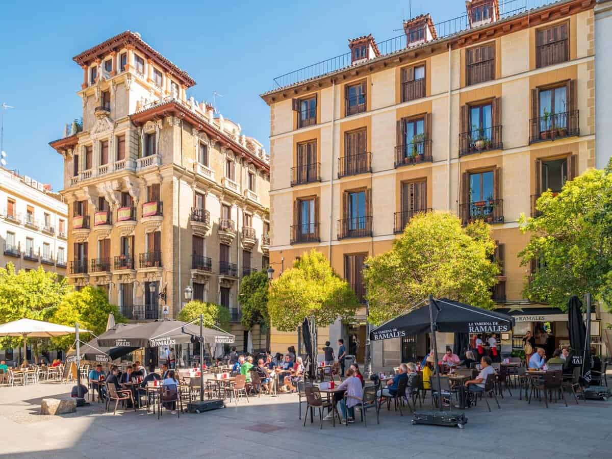 People sit in cafe seating on the street outside on a sunny day.