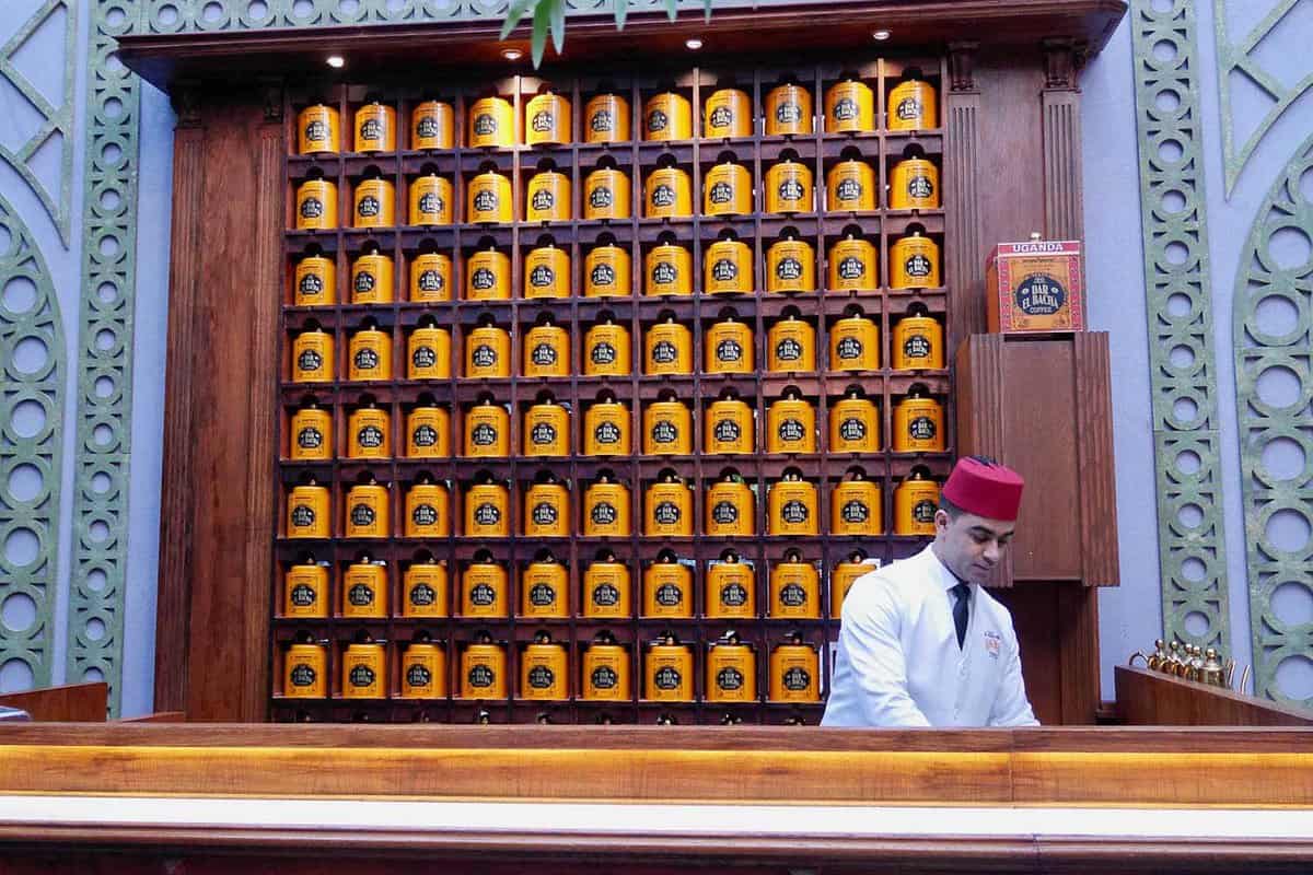 Fez-wearing cafe worker in front of wall covered in tin jars