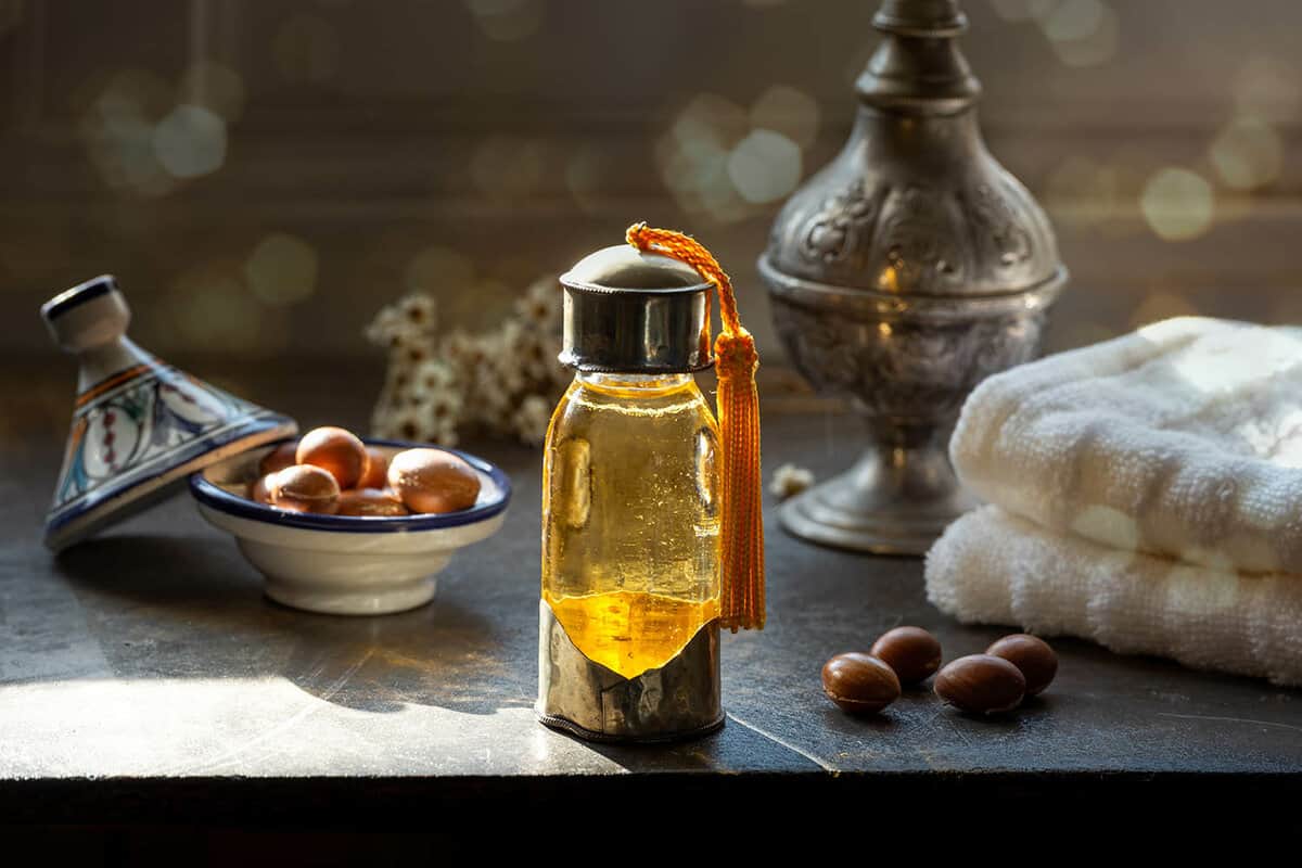 Glass vial containing argan oil next to argan nuts and towels