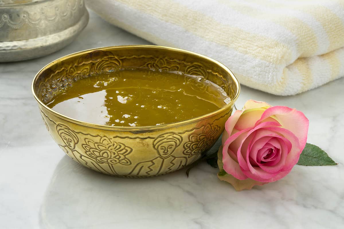 Gold bowl containing brown liquid next to a rose