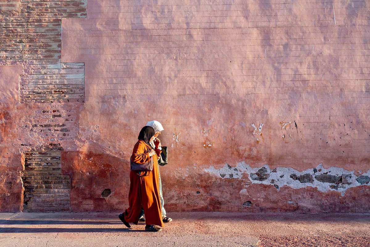 Two women walk in front of pale-pink wall