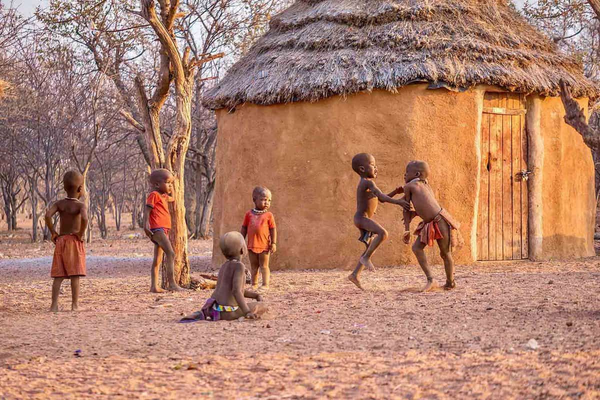 a group of young boys playing together near to a mud hut