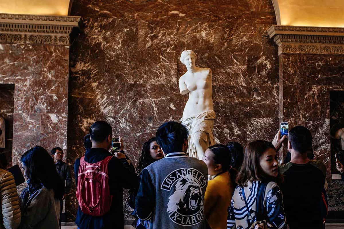 A small crowd in front of the top half of the armless Venus de Milo statue