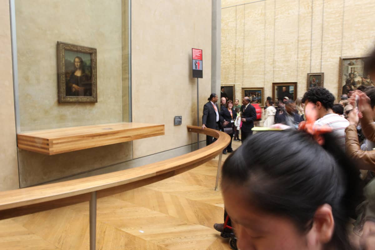 Side view of the Mona Lisa painting being guarded and distanced from onlooking tourists
