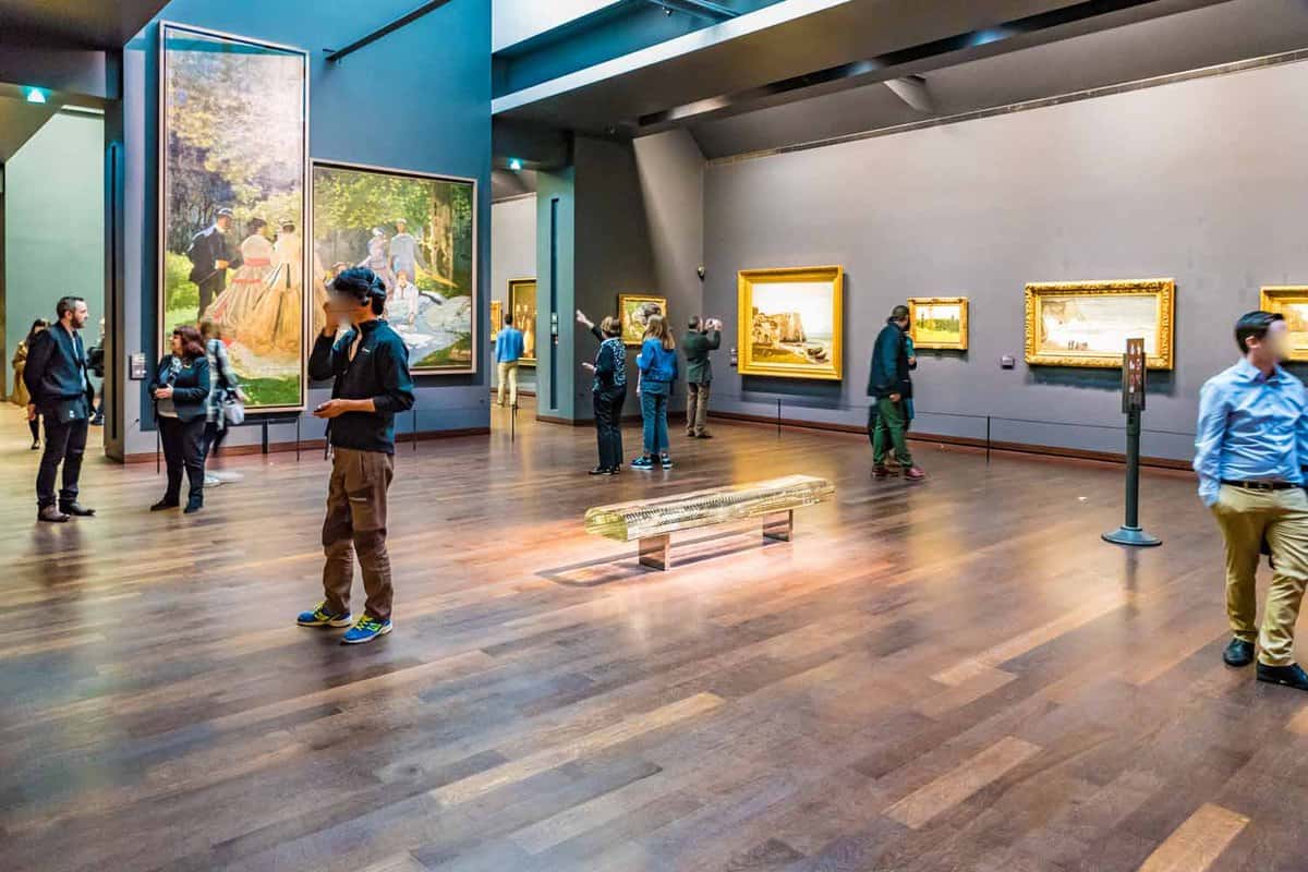 A room inside the museum where there are tourists looking at the paintings around the room
