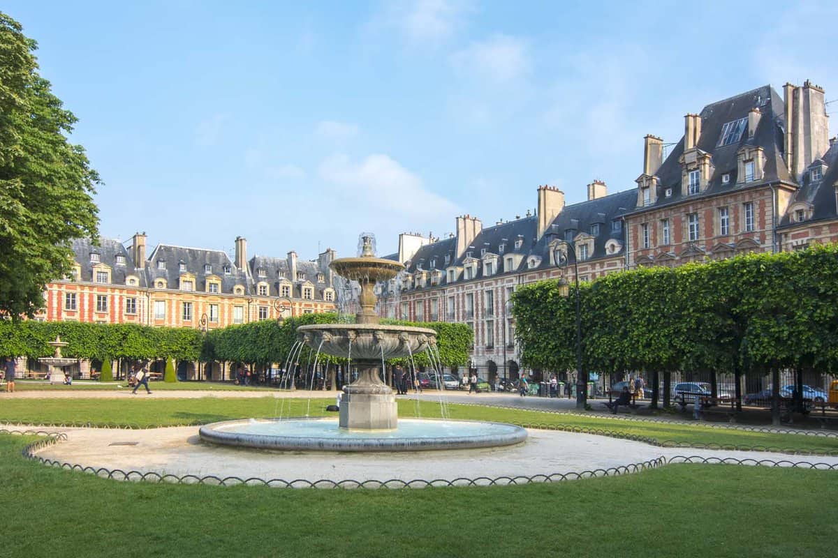 A fountain in Vosges square (Place des Vosges) surrounded by trees and buildings. The square was created in Louis XIII style architecture.