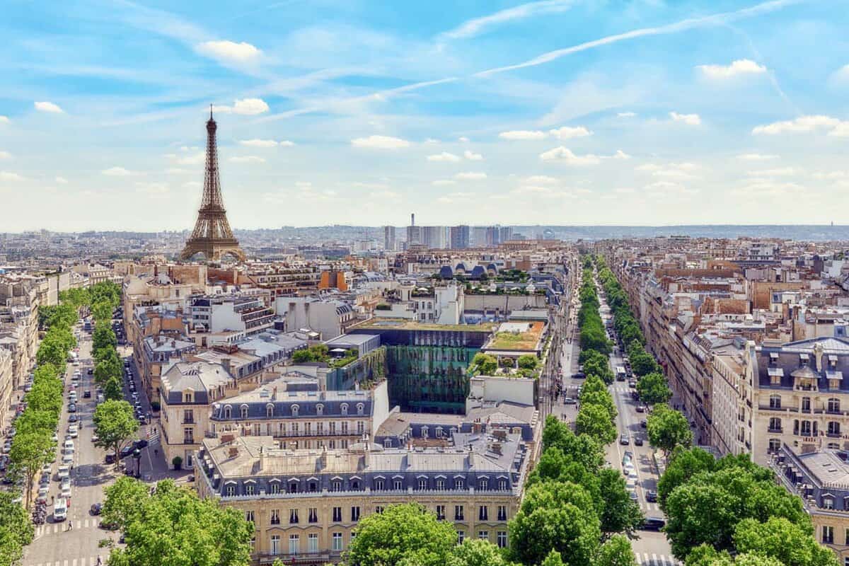 Landscape view of the city, with the Eiffel Tower being in clear view in the far background on a sunny blue yet cloudy day
