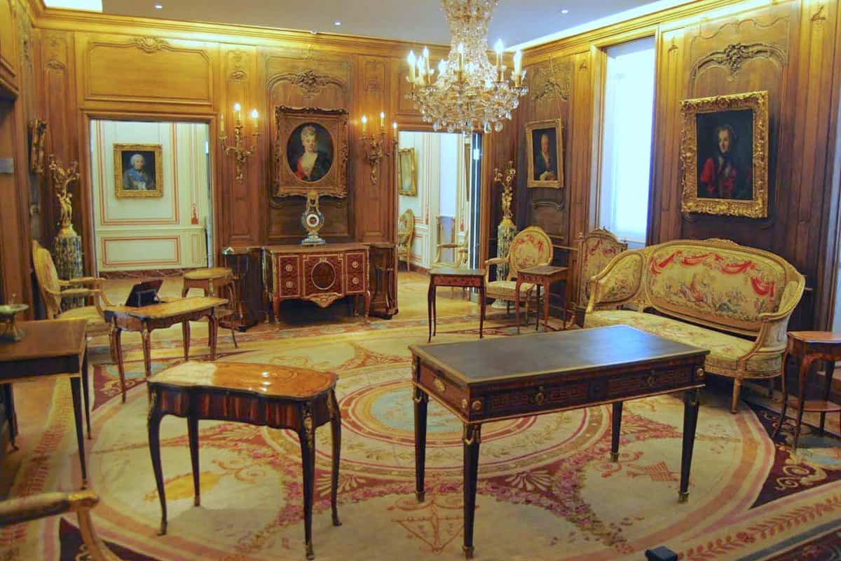 Wagram Room at Musee Cognacq-Jay, filled with wooden polished furniture , paintings on each wall and a chandelier in the centre