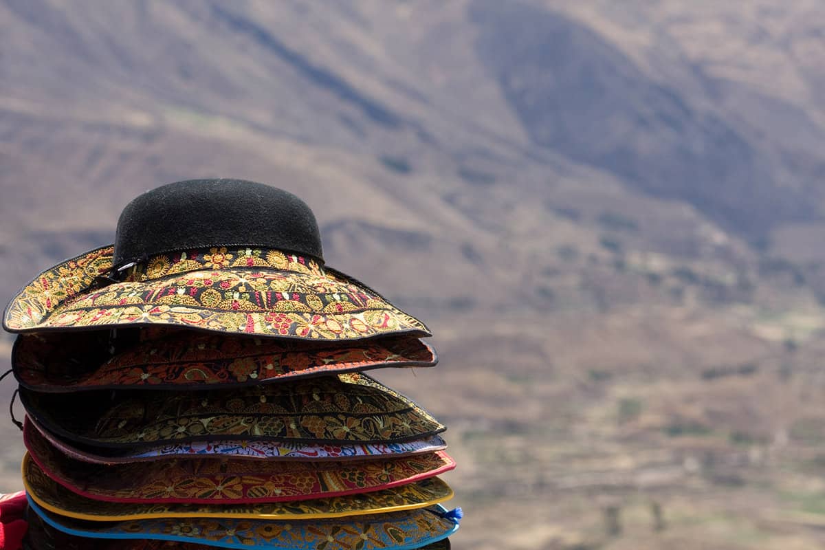 Straw and fabric hats stacked on top of each other, with mountains in the background