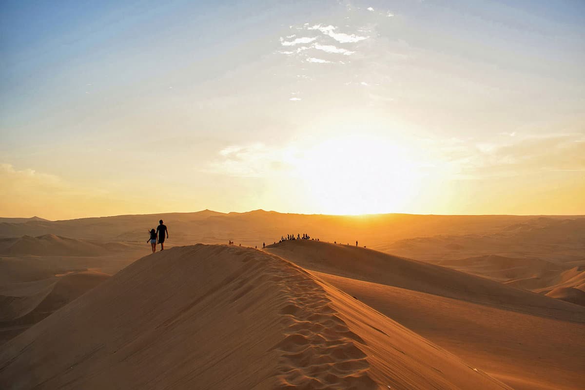 Two people walking along the edge of a sand dune at sunset