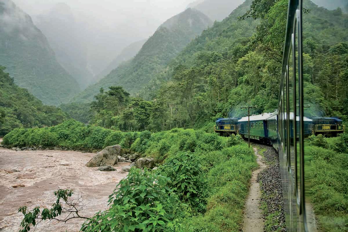 A train winds through misty, lush green mountains