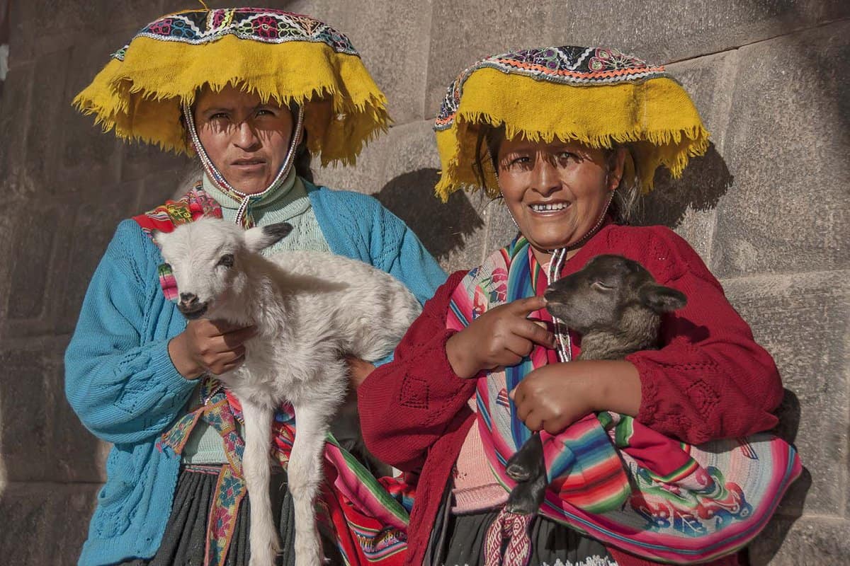 Two women in traditional dress holding lambs