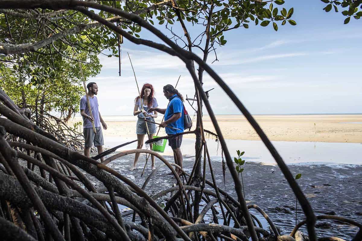 Aboriginal guide with two guests on the beach explaining fishing methods