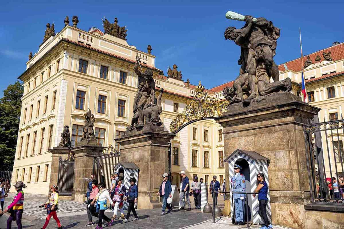 Tourists and guards at the entrance to Prague castle beneath a statue of Fighting Giants.