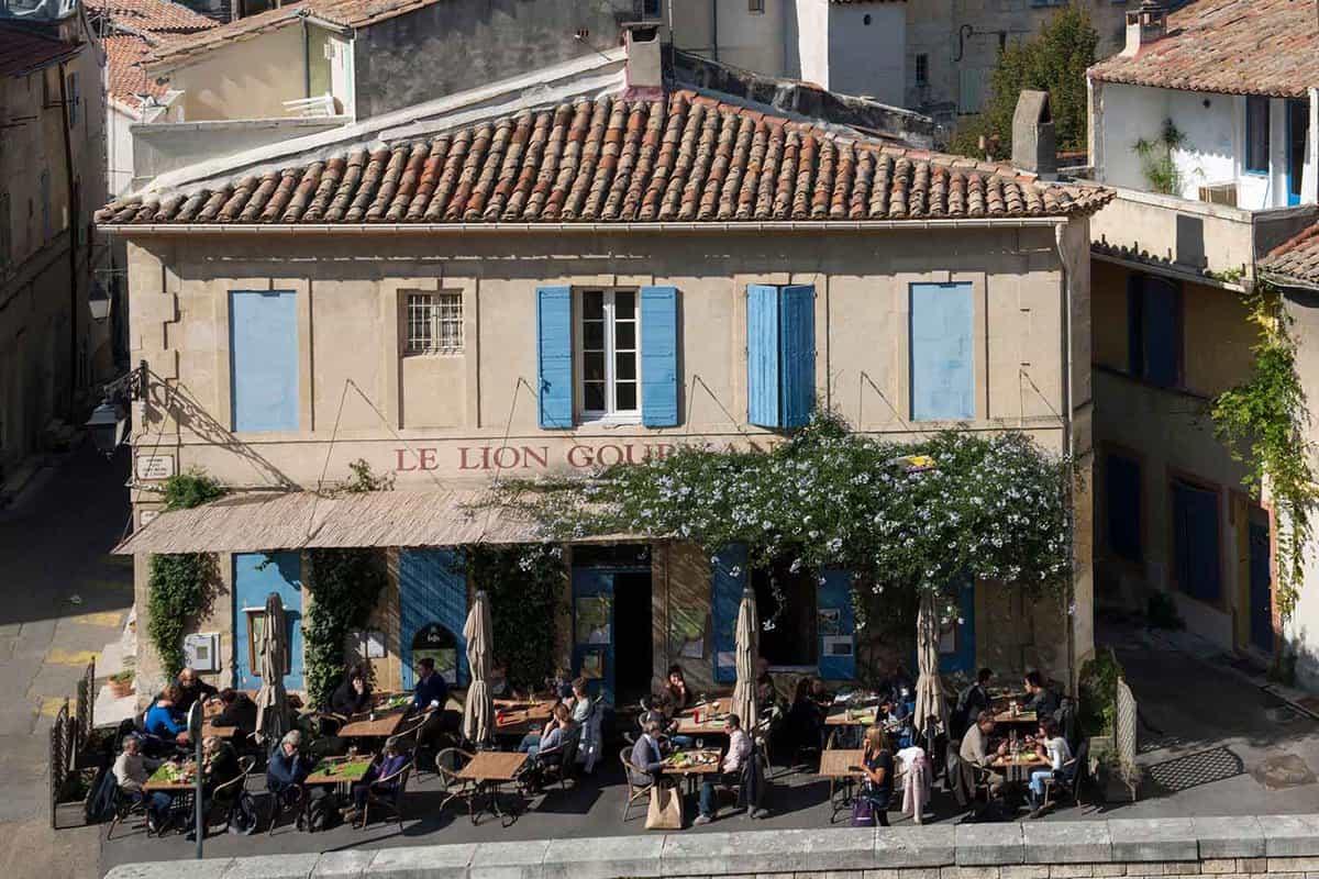 Exterior of Le Lion d'Arles, a restaurant with outdoor seating and blue shutters.