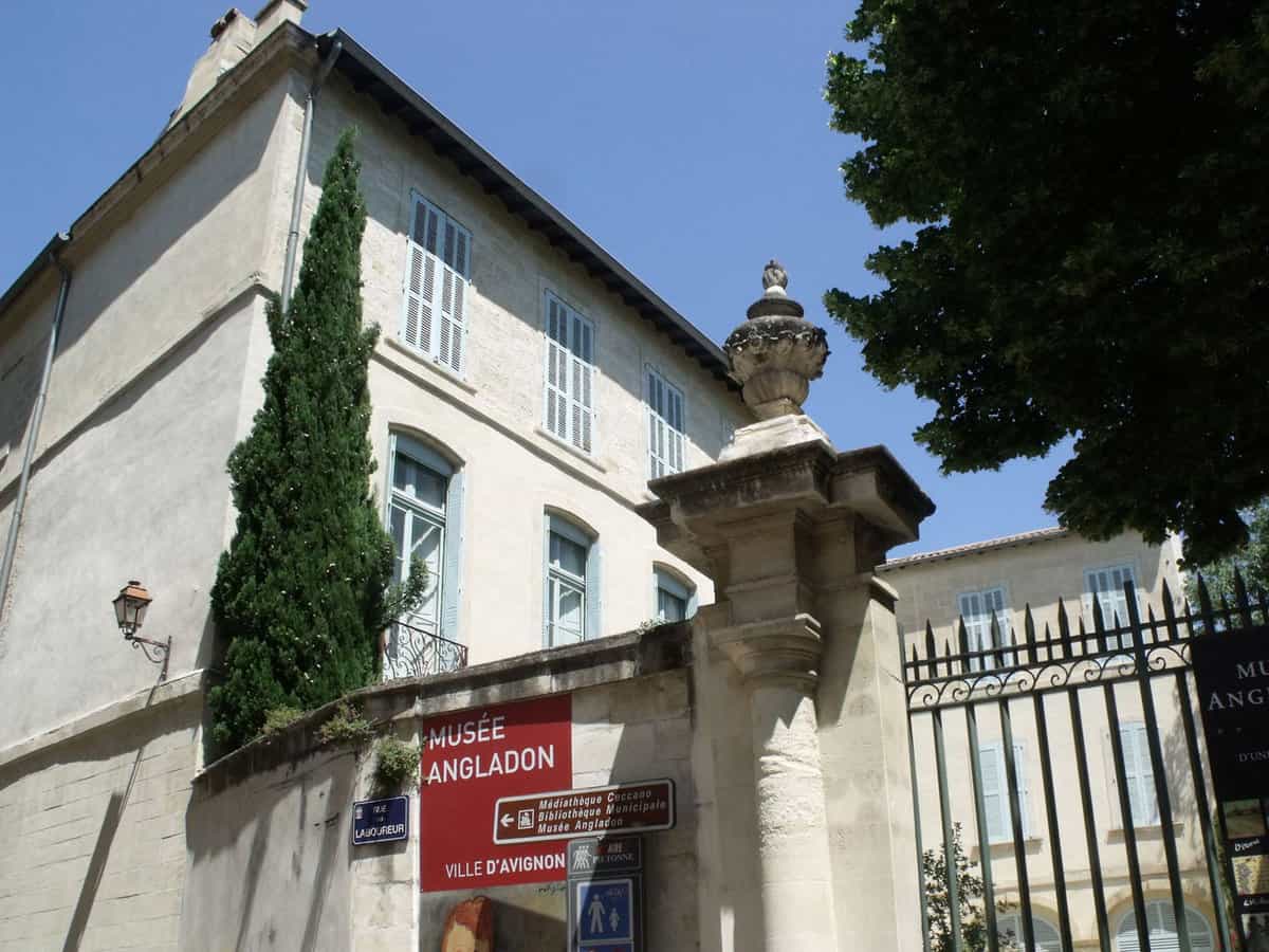 The outside gate of the white stone museum, with a red sign saying 'Musée Angladon'