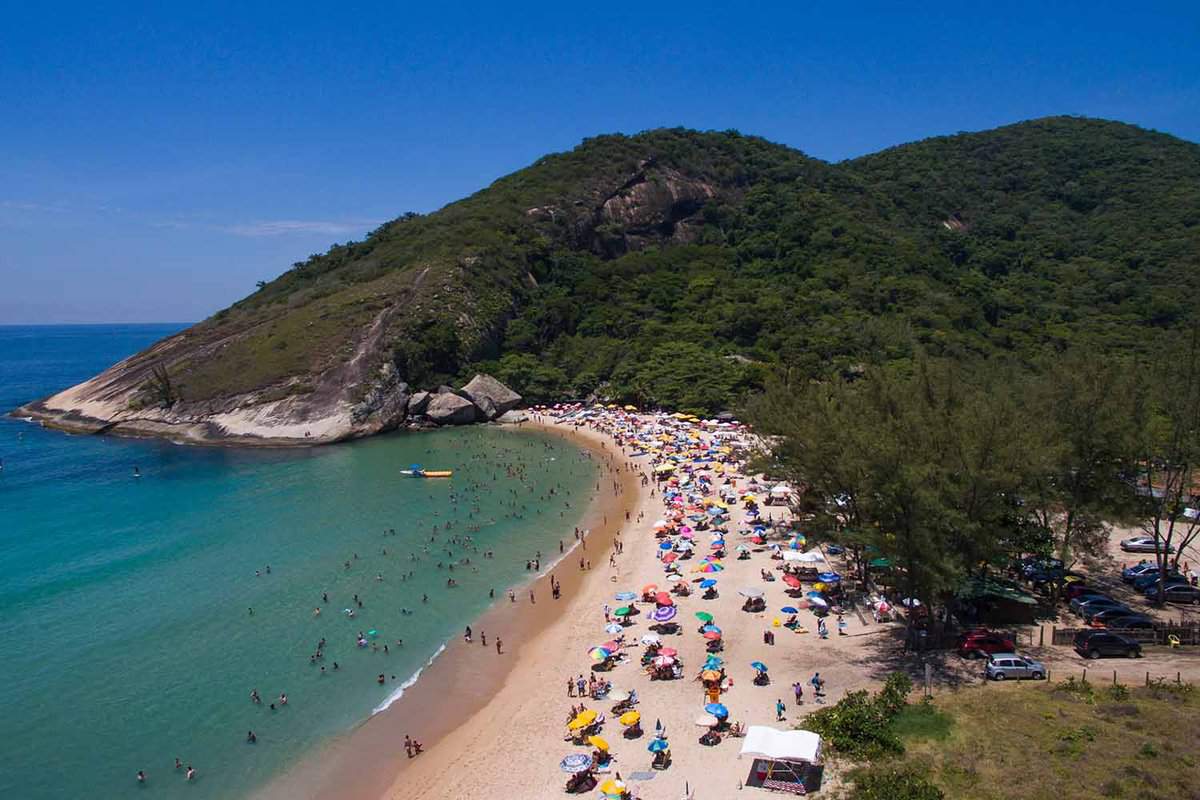 Busy sandy beach with jungle hills in background