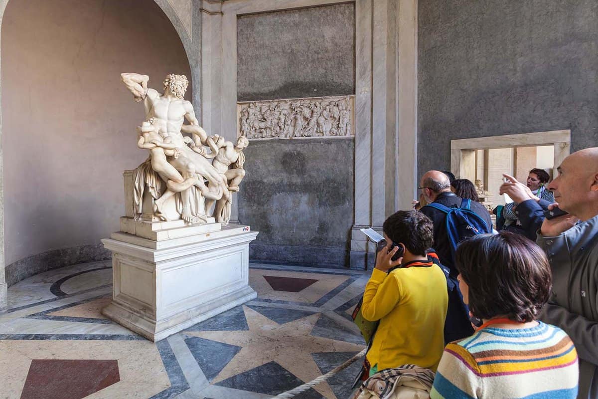 tourists near Laocoon and His Sons (Laocoon Group) ancient sculpture in Gallery of Statues, open loggia of Pio-Clementino Museum