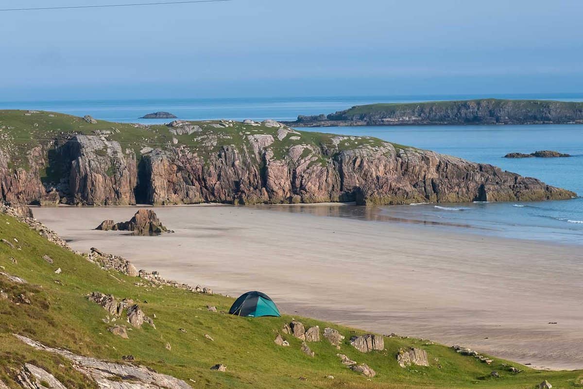Remote beach with golden sand and one small green tent on