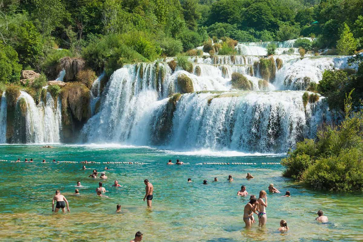 Waterfalls flow into pool with tourists swimming