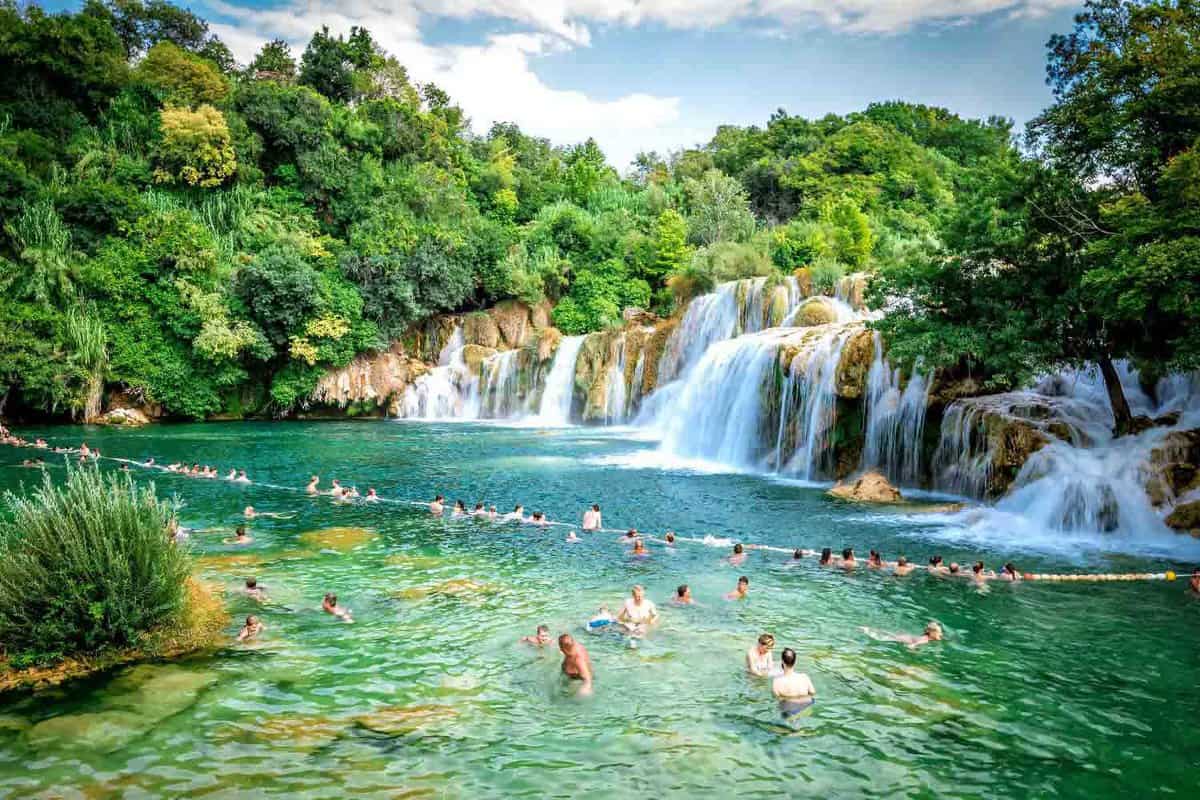 Waterfalls flow into pool with tourists swimming