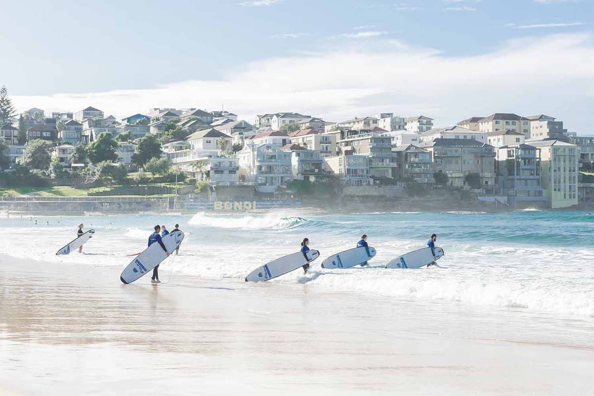 Five people with surf boards walking into the sea on a sunny day.