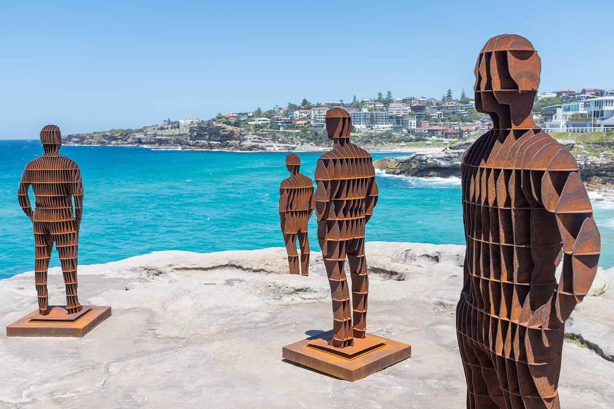 Statues of people looking out in different directions by the sea on a sunny day.