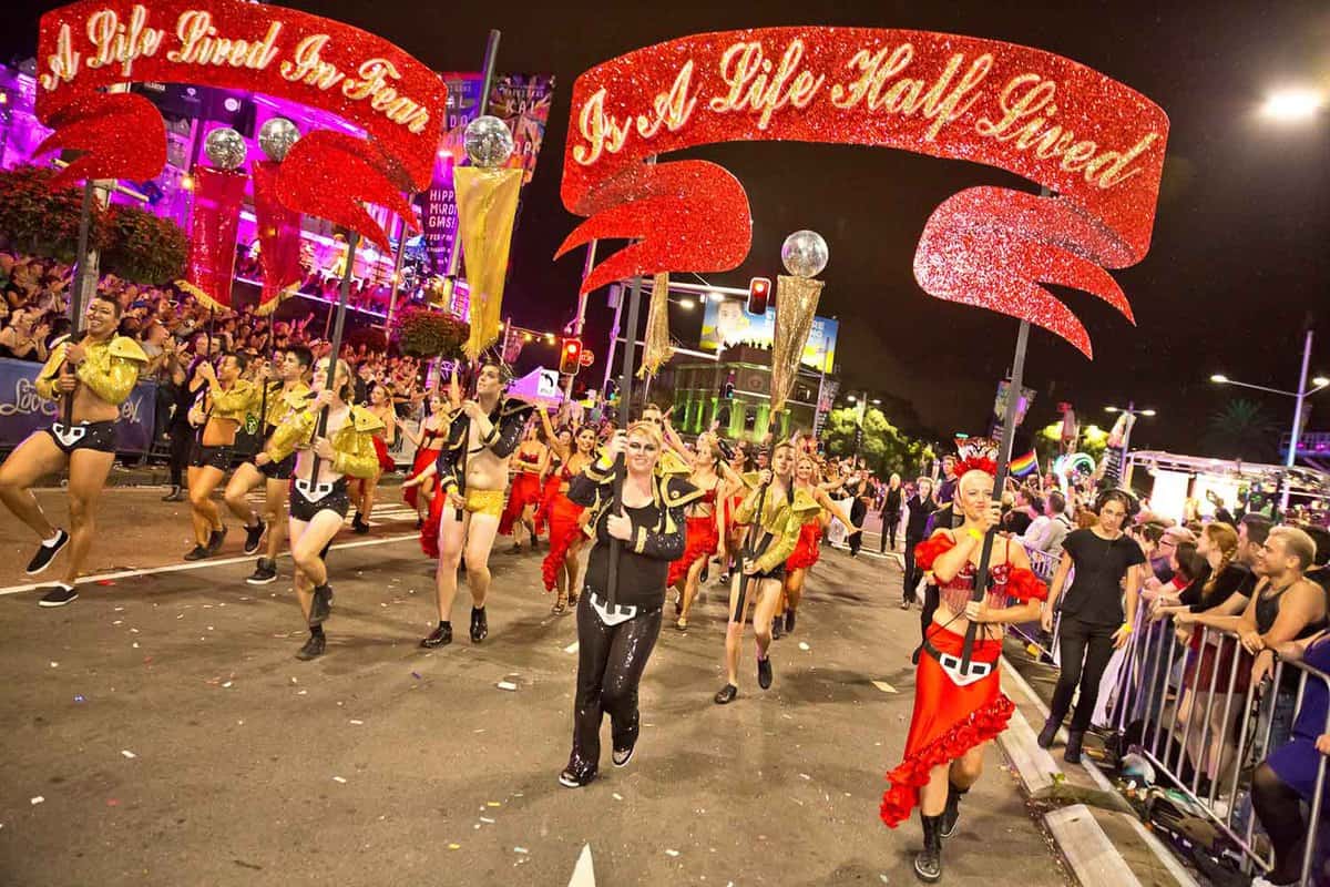 A procession of people wearing vibrant red and yellow costumes as part of the parade. Photo is taken at night.