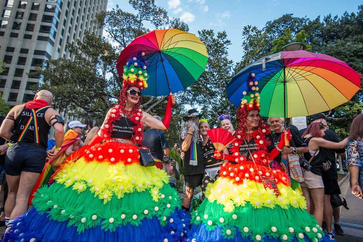 A float with two people in large rainbow dresses, with rainbow umbrellas.