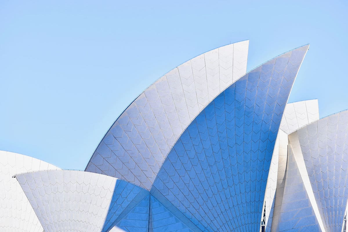 the jagged white sail shaped structure of Sydney Opera House against a blue sky.